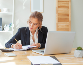 Image of a businesswoman taking notes in front of a laptop.