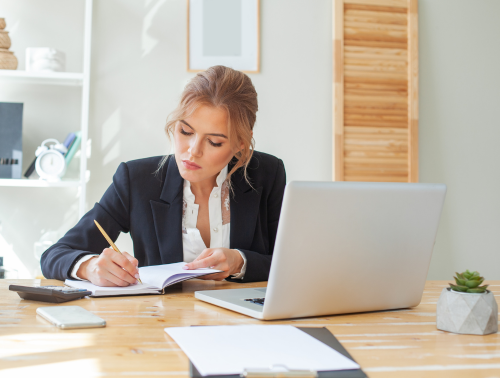 Image of a businesswoman taking notes in front of a laptop.