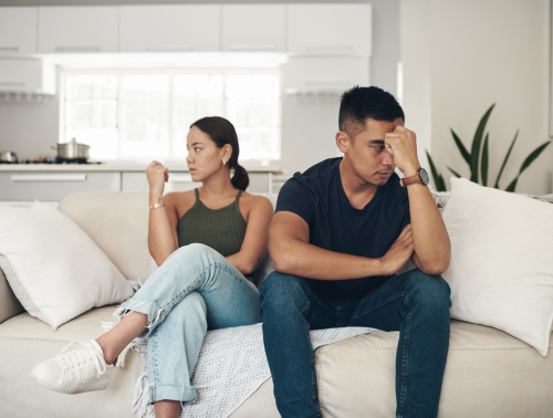 Image of a couple sat on a sofa looking unhappy and turned away from each other.