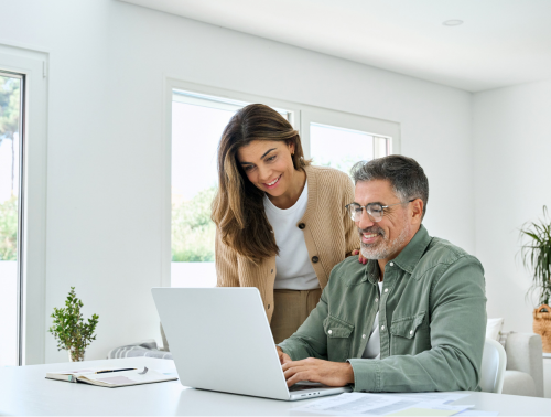 Image of a middle-aged man working on a laptop next to a woman, representing will preparation.