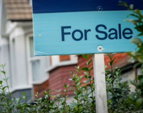 Image of a "For Sale" sign in front of a property on a residential street.