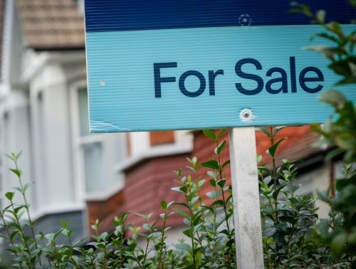 Image of a "For Sale" sign in front of a property on a residential street.