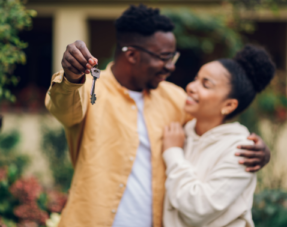 Image of a happy couple, one with a set of house keys, representing buying a home.