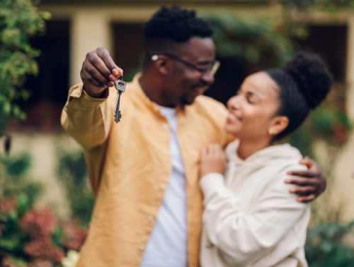Image of a happy couple, one with a set of house keys, representing buying a home.