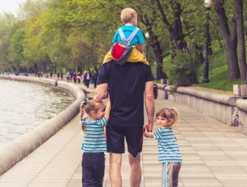 Photo of a man with three children walking next to a river.