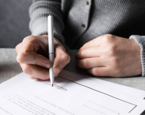 Woman signing a document at a grey table.