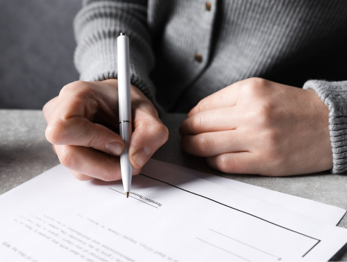 Woman signing a document at a grey table.