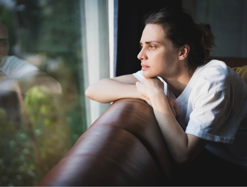 A woman sitting on a couch, looking thoughtfully out a window.