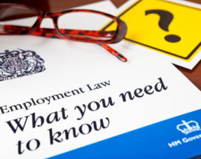 Employment Law guide sitting on a desk alongside a pair of reading glasses and a yellow card featuring a question mark.