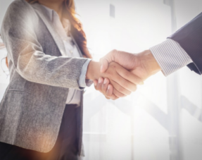 A close-up shot of two business professional people shaking hands in a bright office environment.