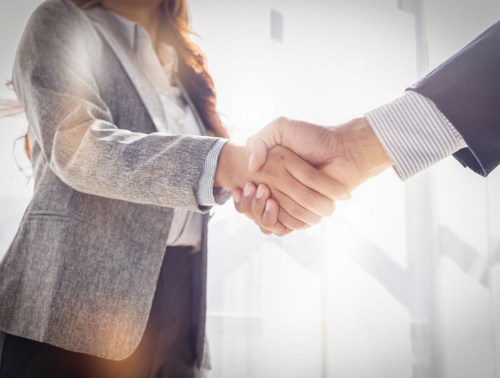 A close-up shot of two business professional people shaking hands in a bright office environment.